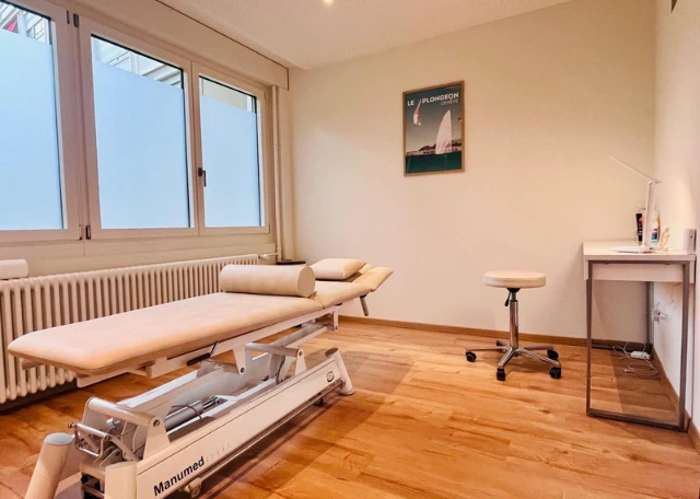 photo d'une cabine de soin avec une table de physiothérapeute beige manumed comme indiaue sur le pied avec un cadre geneva. Il s'agit d'une cabine de physiotherapie du centre Helvetic Physio à Geneve